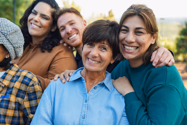 Group of diverse adults smiling and posing closely outdoors.