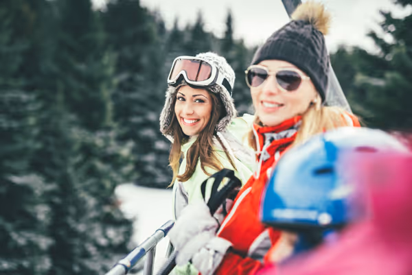 Two women dressed in winter gear smiling outdoors with snow-covered trees in the background.