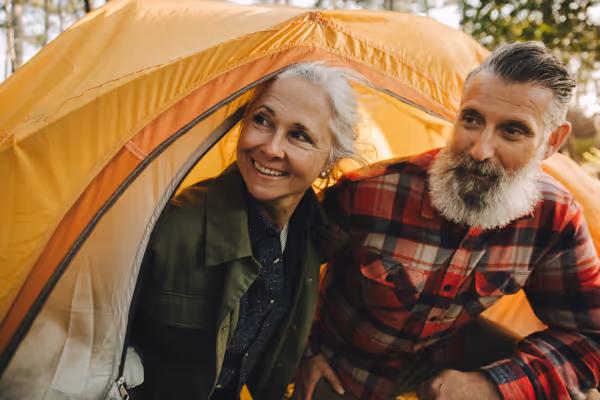 Smiling older couple sitting inside an orange camping tent in a wooded area.
