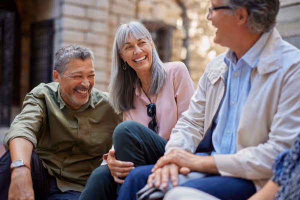 Three older adults sitting together outdoors, smiling and enjoying a conversation.