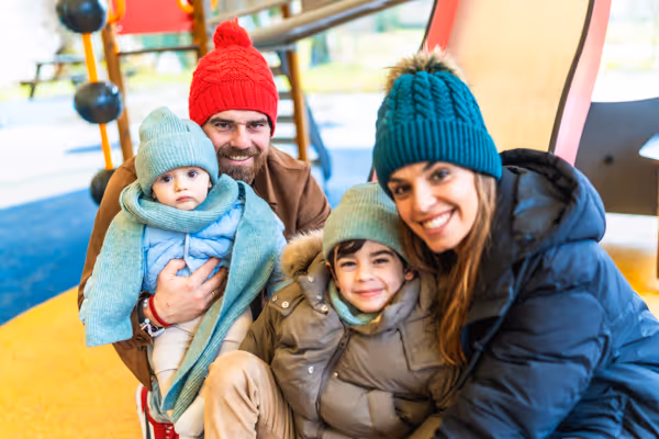 Smiling family of four wearing winter clothes, posing together at a playground.