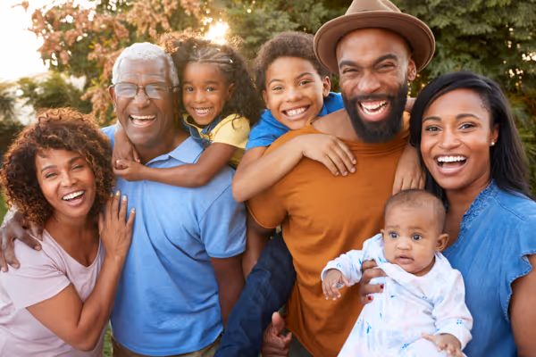 Smiling multigenerational Black family outdoors with two children and a baby, enjoying a sunny day.