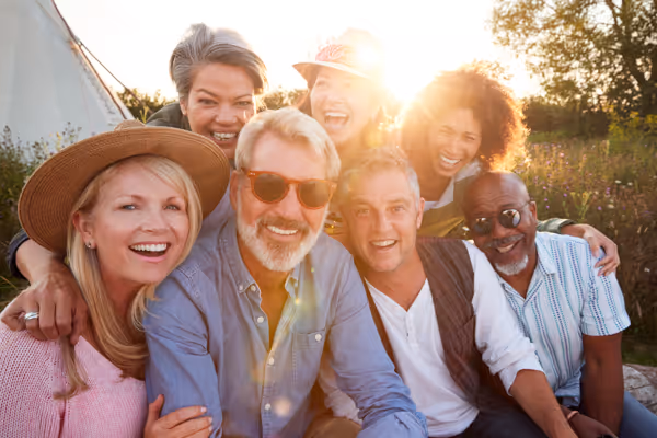 Group of six diverse adults smiling and sitting closely together outdoors in natural light.